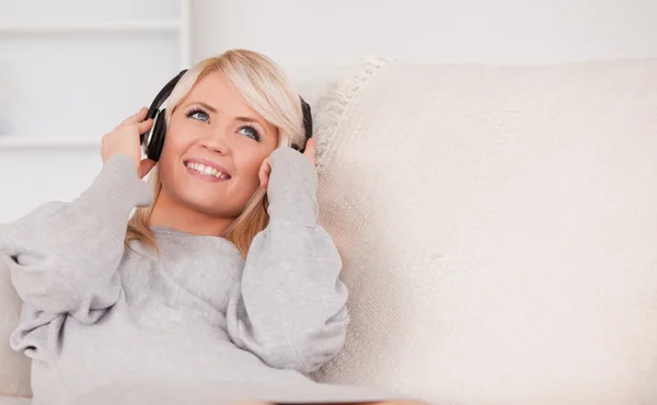 ソファーで横になっているヘッドフォンで美しい金髪の女性 — ストック写真