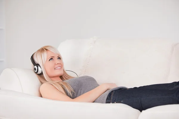 Χαμογελαστός νεαρός ξανθιά γυναίκα με ακουστικά ξαπλωμένη σε έναν καναπέ — Φωτογραφία Αρχείου