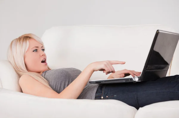 惊讶的女人放松在笔记本电脑上躺在一张沙发上 — 图库照片