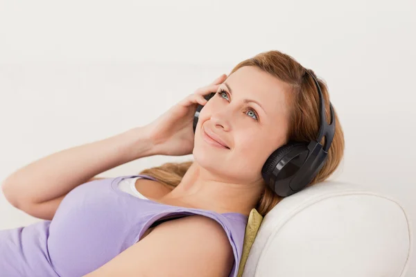 Sorridente donna dai capelli biondi che ascolta musica sdraiata sul divano — Foto Stock