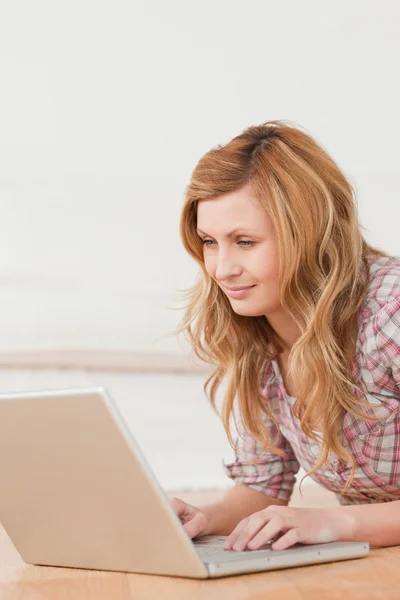 Blonde woman working on her laptop lying down on the floor — Stock Photo, Image