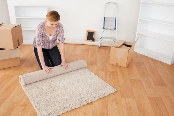 Niedliche Frau rollt einen Teppich aus, um sich auf den Umzug vorzubereiten — Stockfoto