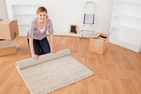 Mujer atractiva enrollando una alfombra para prepararse para mudarse de casa — Foto de Stock