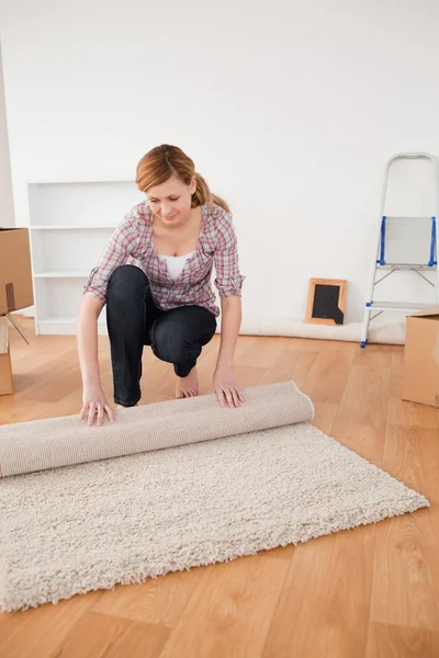 Vacker kvinna rullar upp en matta att förbereda för att flytta hus — Stockfoto