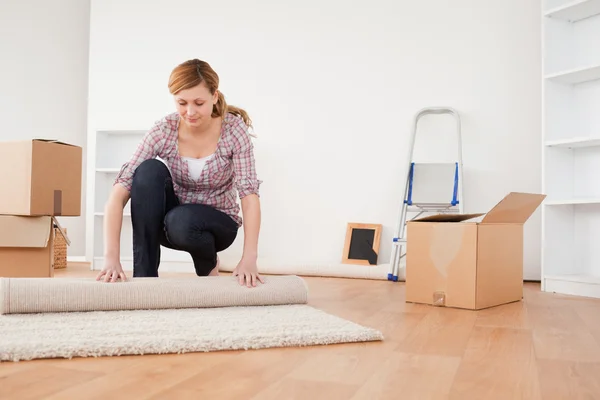 Härlig kvinna rullar upp en matta att förbereda sig för att flytta hus — Stockfoto