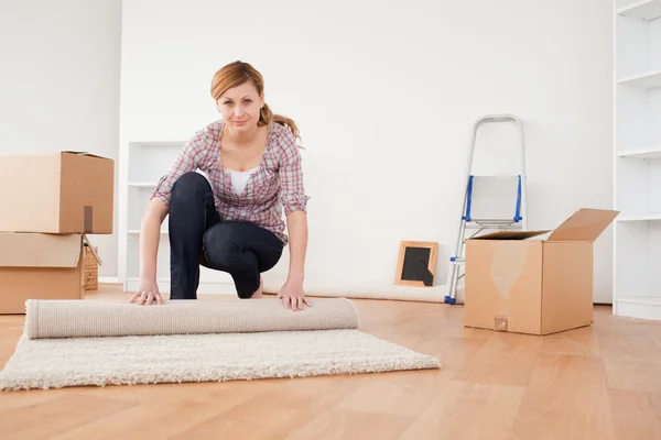 Ładny blond kobieta toczenia się dywan do przygotowań do przeniesienia domu — Zdjęcie stockowe
