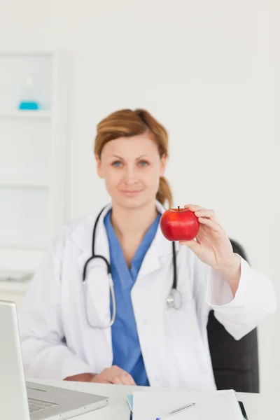 Cute female doctor showing a red apple to the camera in her surg — Stock Photo, Image