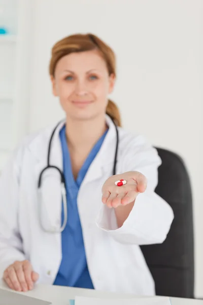 Blonďatí doktor ukazující pilulky s kamerou — Stockfoto