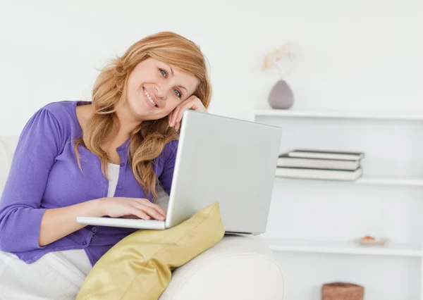 Mujer feliz sonriente sentada en el sofá y usando una computadora portátil — Foto de Stock