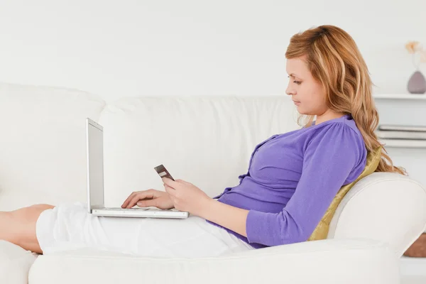 Mulher ruiva bonita usando um laptop e telefone enquanto está deitado — Fotografia de Stock