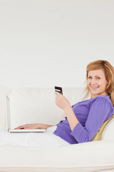 Mujer pelirroja sonriente usando una computadora portátil y un teléfono mientras miente —  Fotos de Stock