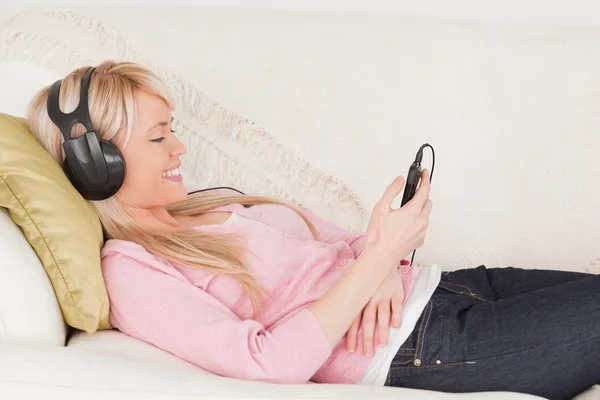 Hermosa mujer escuchando música en sus auriculares mientras miente —  Fotos de Stock