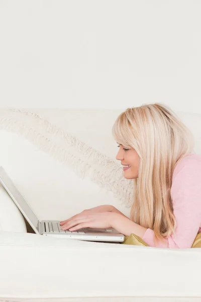 Giovane bionda femminile rilassante con un computer portatile mentre si trova su un divano — Foto Stock