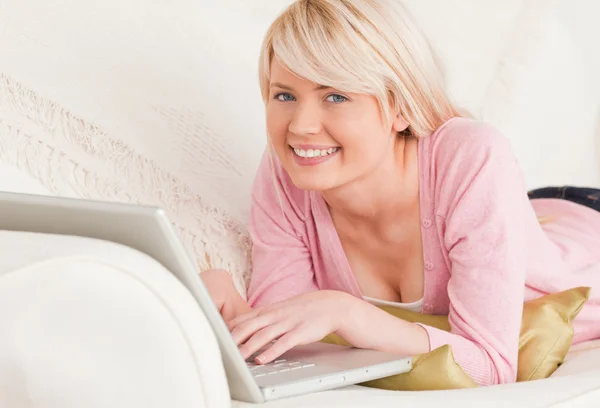 Joven mujer atractiva relajarse con un ordenador portátil mientras está acostado en un —  Fotos de Stock