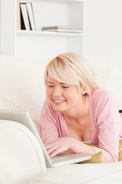 Joven mujer de buen aspecto relajarse con un ordenador portátil mientras está acostado —  Fotos de Stock