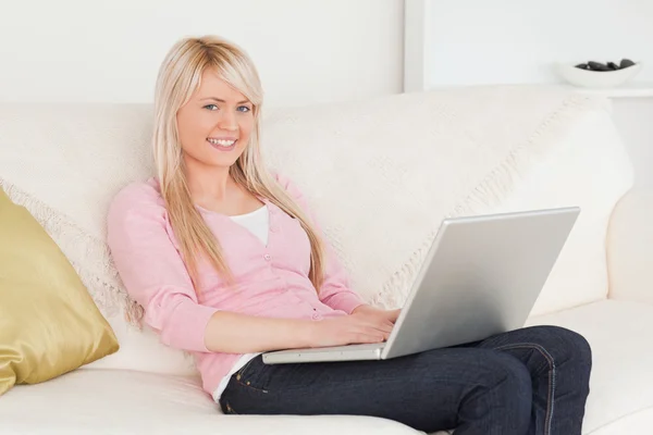 Joven mujer sonriente relajarse con un ordenador portátil mientras está sentado en un s — Foto de Stock