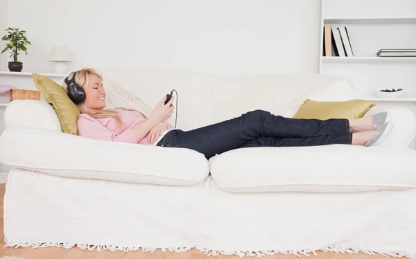 Hübsche Frau hört Musik über Kopfhörer, während sie auf dem Bett liegt — Stockfoto