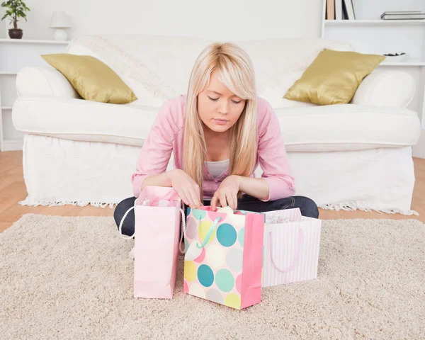 Kendi alışveriş torbaları ile oturma odasında oturan sarışın kadın — Stok fotoğraf