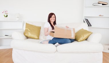 Beautiful red-haired female opening a carboard box while sitting clipart