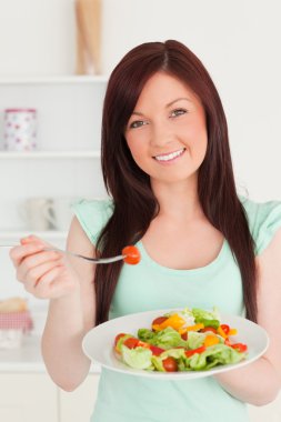 Good looking red-haired woman enjoying a mixed salad in the kitc clipart