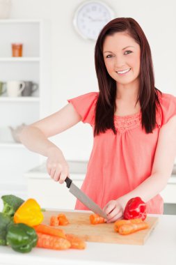 Beautiful red-haired woman cutting some carrots in the kitchen clipart