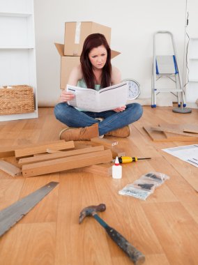 Gorgeous red-haired female reading a manual before do-it-yoursel clipart