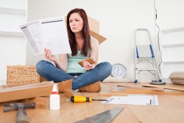 Lovely red-haired female reading a manual before do-it-yourself clipart