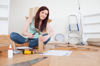 Beautiful red-haired female nailing a plank at home clipart