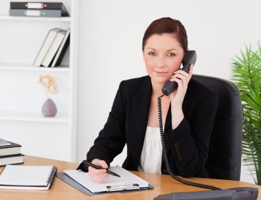 Young beautiful red-haired woman in suit writing on a notepad an clipart