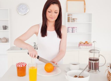 Young good looking red-haired woman cutting an orange in the kit clipart