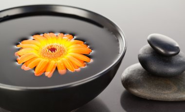 Orange flower floating on a black bowl and a stack of black pebb clipart