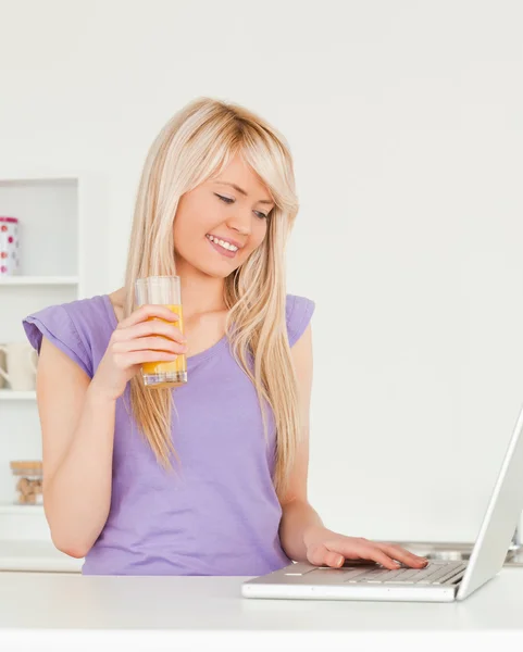 Hermosa mujer bebiendo jugo de naranja y relajarse en un ordenador portátil i —  Fotos de Stock
