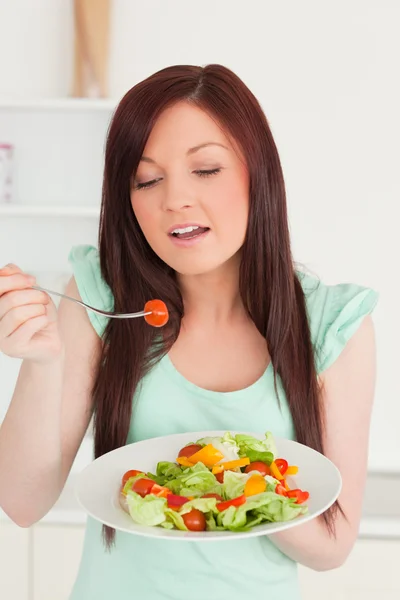 Mulher ruiva gostando de uma salada mista na cozinha — Fotografia de Stock