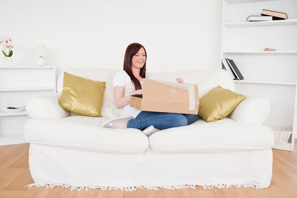 Atractiva hembra pelirroja abriendo una caja de cartón mientras está sentada — Foto de Stock