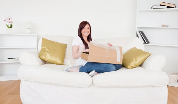 Bella donna dai capelli rossi che apre una scatola di cartone mentre è seduta — Foto Stock