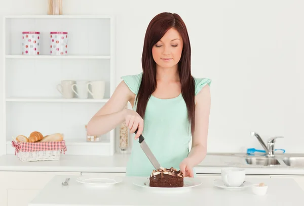 Szép, vörös hajú nő vágás néhány süteményt, a konyhában — Stock Fotó
