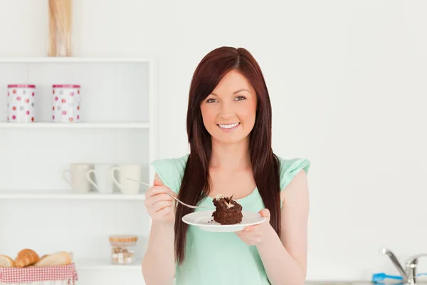 Jó látszó vörös hajú nő eszik néhány a torta, a konyhában — Stock Fotó