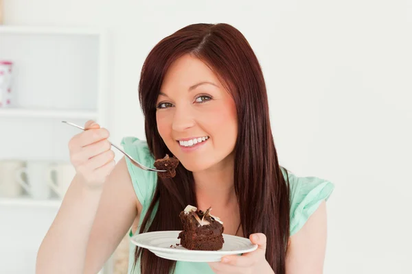 Χαριτωμένο κοκκινομάλλης γυναίκα τρώει κάποια κέικ στην κουζίνα — Φωτογραφία Αρχείου