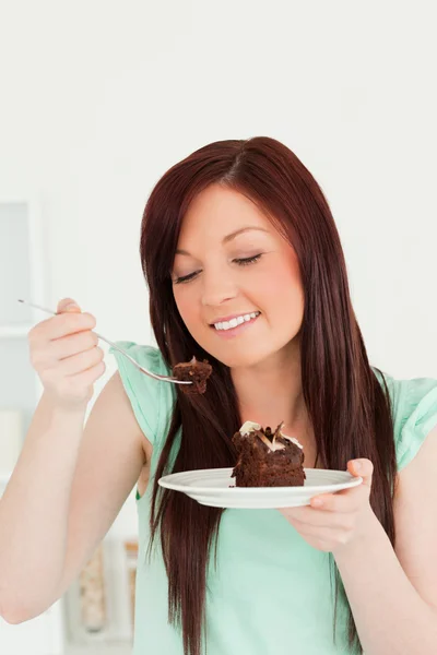 Радостная рыжая женщина ест торт на кухне. — стоковое фото