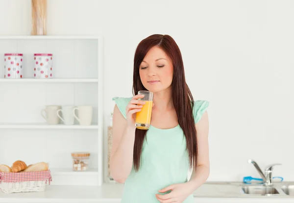 Atractiva mujer pelirroja disfrutando de un vaso de jugo de naranja en — Foto de Stock
