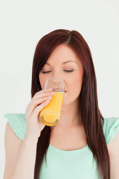 Attractive red-haired woman drinking a glass of orange juice in — Stock Photo, Image