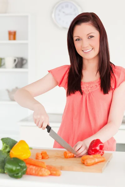 Gyönyörű vörös hajú nő vágás néhány sárgarépát, a konyhában — Stock Fotó