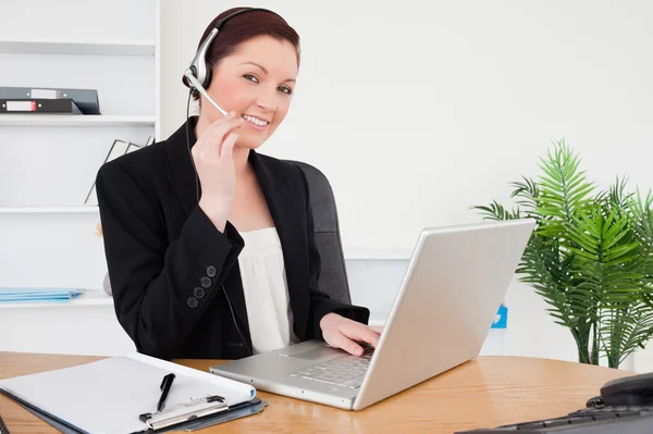 Young attractive red-haired female in suit typing on her laptop — Stock Photo, Image
