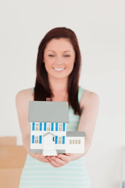 Mujer bastante pelirroja sosteniendo una casa en miniatura mientras está de pie —  Fotos de Stock