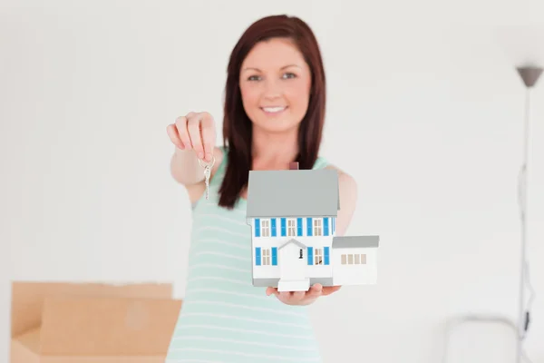 Good looking red-haired female holding a miniature house while s — Stock Photo, Image