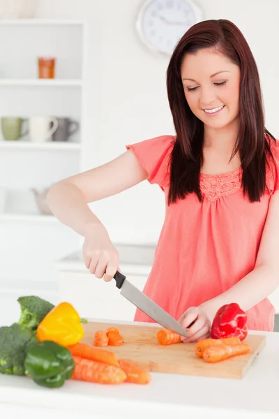Aantrekkelijke roodharige vrouw snijden sommige wortelen in de keuken — Stockfoto
