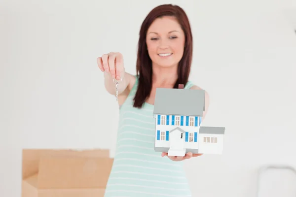 Bastante pelirroja hembra sosteniendo una casa en miniatura mientras de pie — Foto de Stock