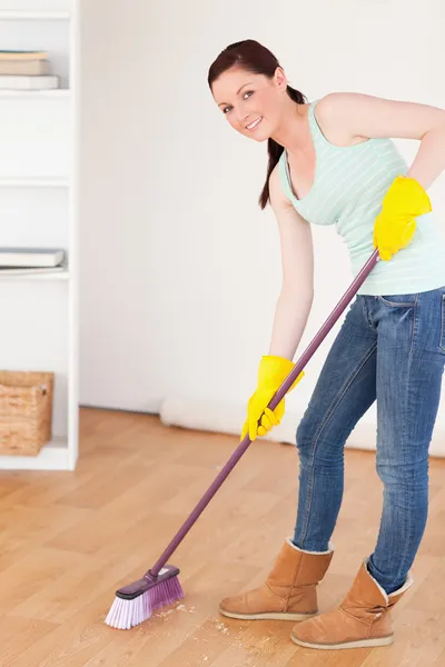 Bra lookingl rödhårig kvinna sopa golvet hemma — Stockfoto