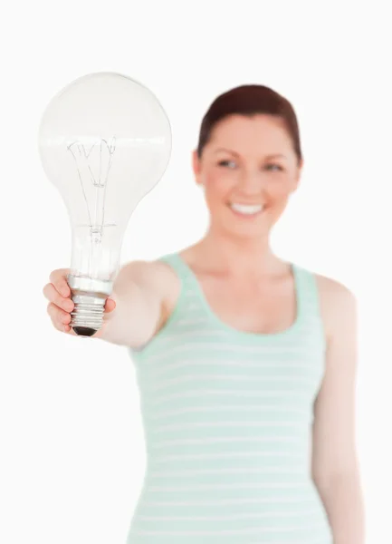 Досить рудоволоса жінка тримає лампочку, стоячи — стокове фото