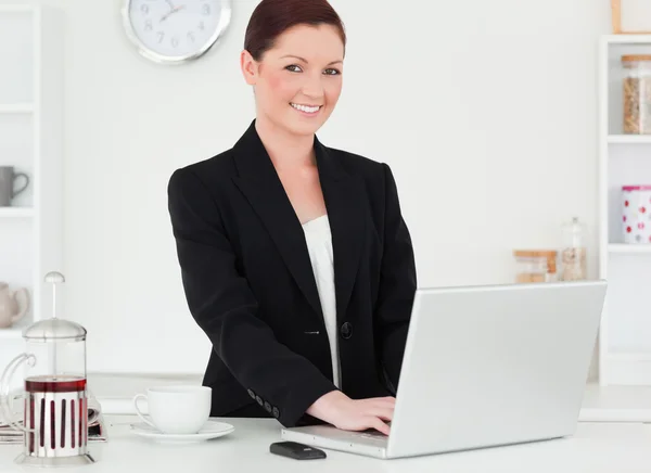 Pretty red-haired woman in suit relaxing with her laptop while p — Stock Photo, Image
